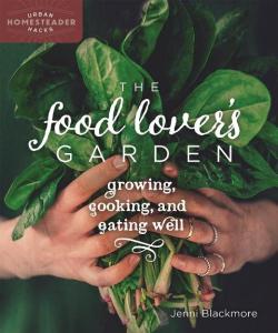 book cover of The Food Lover's Garden Shows two hands holding a bunch of fresh picked greens, possibly spinach or tatsoi.